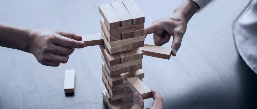 Two individuals engaged in play, stacking wooden blocks on a table, showcasing creativity and collaboration, refer to forex trade plan and mistakes