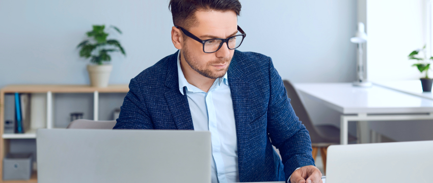 A man in glasses is engaged in forex trade analysis on his laptop, concentrating on his tasks.