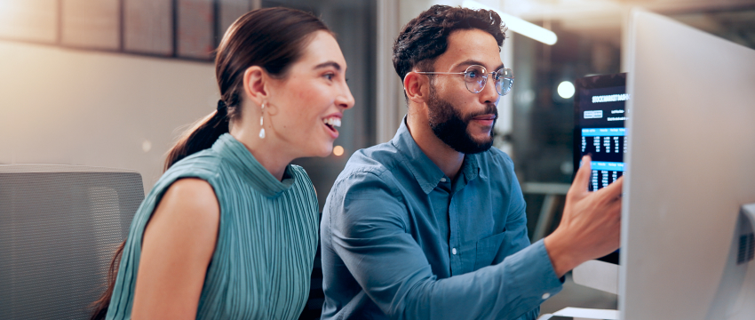 A man and a woman collaborate at a computer in a modern office forex traders. The man points at the screen displaying data, as hobby trading while the woman looks on, smiling.