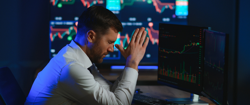 A trader man sitting at a desk, hands on his head, contemplating how to overcome fear in trading.