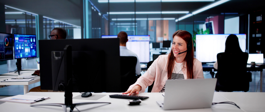 A woman with a headset is concentrated on her computer, actively learning to trade with discipline and focus.